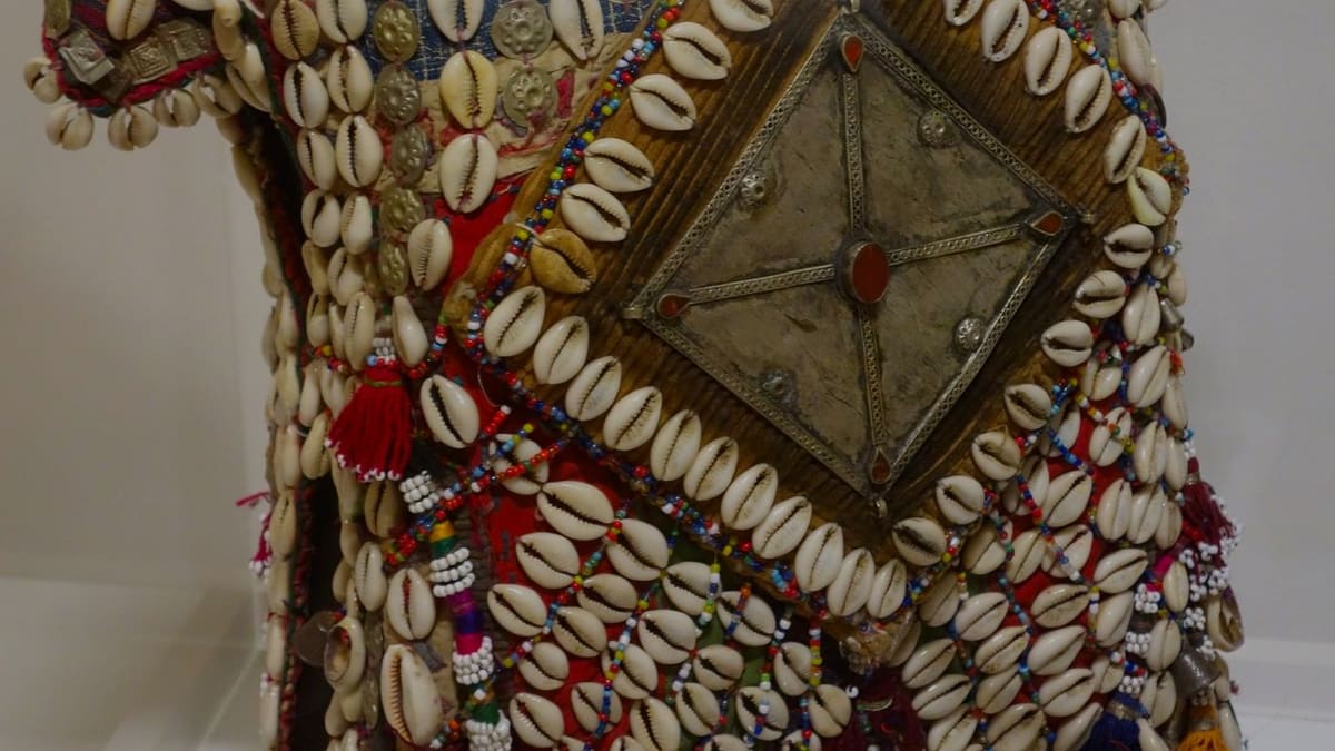 Objet de tradition africaine orné de cauris, posé sur une étoffe claire